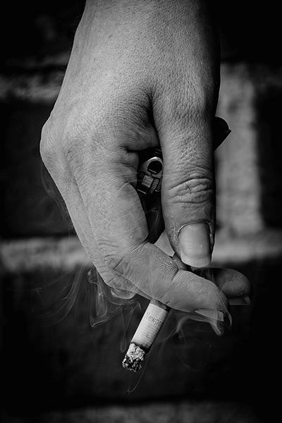 A monochrome photo of a person’s hand holding a lit cigarette and lighter.