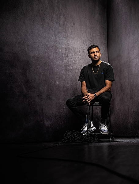 An example of the power of lighting and shadows in photography showing a person sits on a metal stool against a dark, textured background while looking slightly away from the camera with a serious expression.