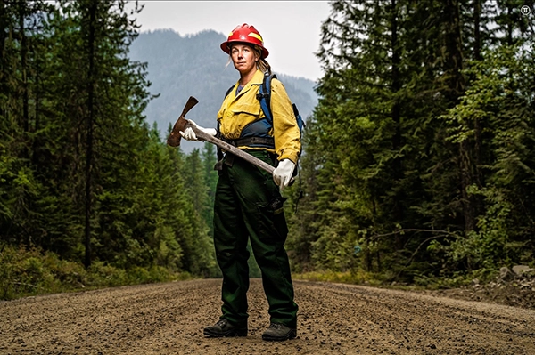 A forestry worker shot with cinematic lighting for photography confidently stands in the middle of a dirt road with dense forest in the background.