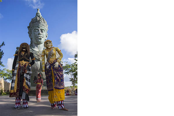Photo of a Woman with Two Giant Wearing a Costume and a Statue Behind Them Shot by Tamron 18-400mm Lenses
