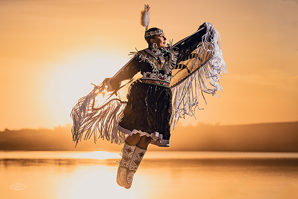 Tribal dancer jumping above river at sunset